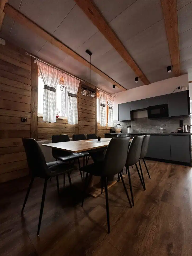 Przestronna jadalnia połączona z kuchnią w apartamencie Karino, Vigor Horses, z drewnianym stołem, czarnymi krzesłami i klimatycznym oświetleniem nad stołem