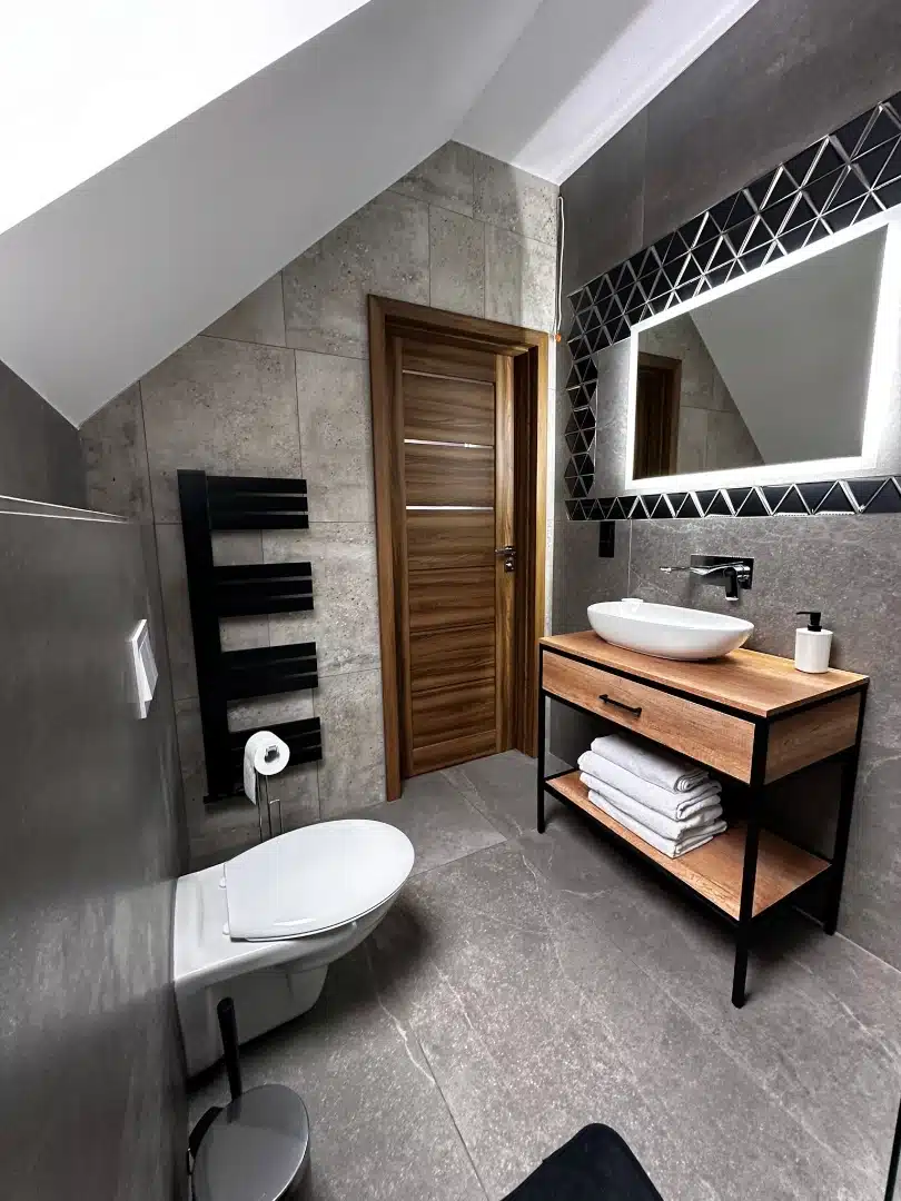 Elegancka łazienka w apartamencie Karino, Vigor Horses, z nowoczesną umywalką na drewnianej szafce, dużym lustrzanym odbiciem i designerskim oświetleniem
