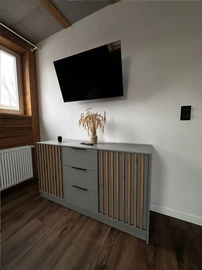 Część wypoczynkowa w apartamencie Karino, Vigor Horses, z telewizorem naściennym i stylową szafką w odcieniach szarości z drewnianymi elementami