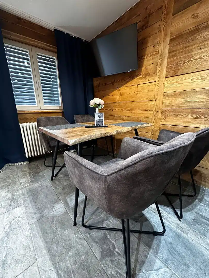 Widok ogólny jadalni w apartamencie Legia, Vigor Horses, z drewnianym stołem i komfortowymi, szarymi krzesłami, idealne miejsce na spokojne posiłki z rodziną czy przyjaciółmi