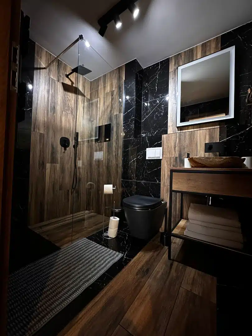 Łazienka w apartamencie Legia, Vigor Horses, z połączeniem drewnianych i marmurowych wykończeń, nowoczesnym prysznicem bez brodzika i stylową umywalką na drewnianym blacie
