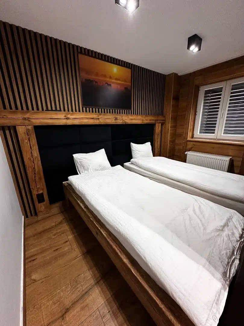 Sypialnia z podwójnym łóżkiem w apartamencie Legia, Vigor Horses, charakteryzująca się drewnianym wykończeniem i dekoracyjnym obrazem przedstawiającym konie przy zachodzie słońca, zapewniającym ciepłą atmosferę