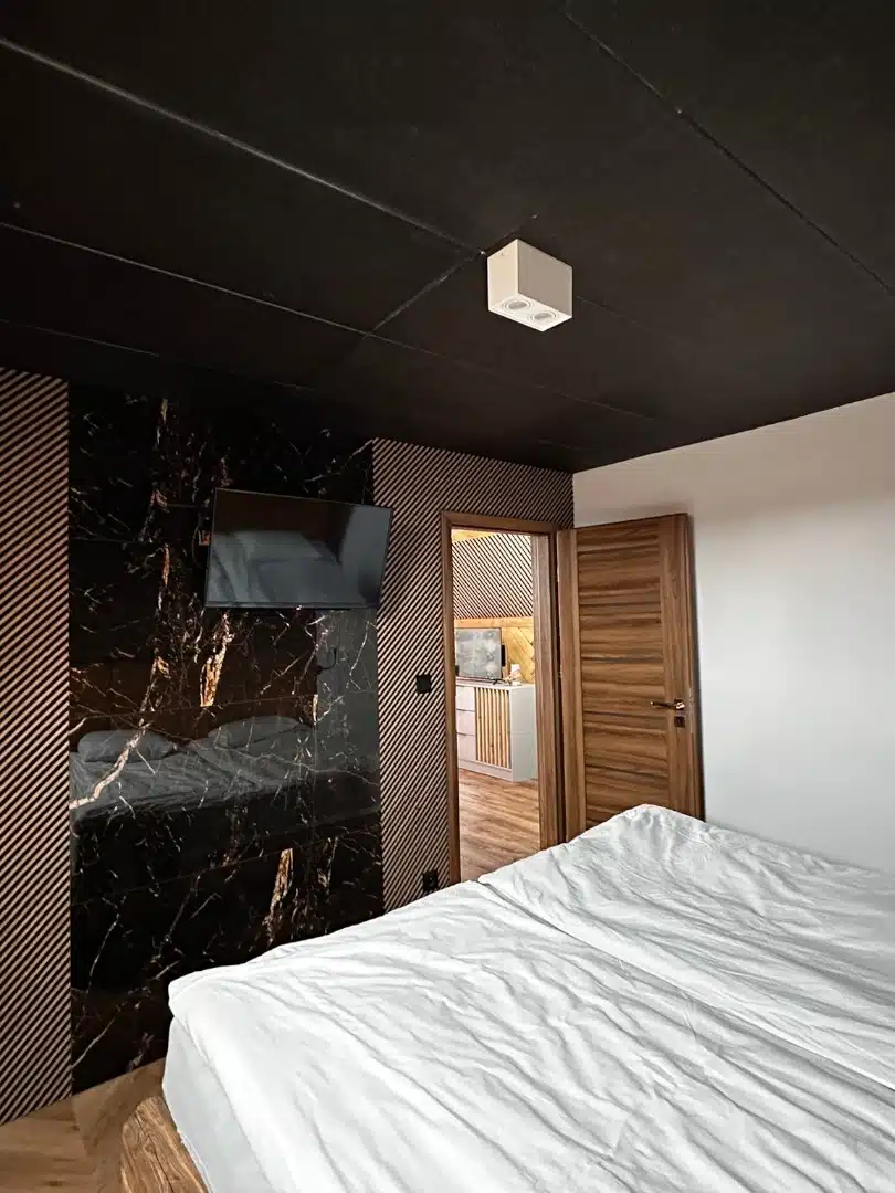 Elegancka sypialnia w apartamencie Merida, Vigor Horses, z wielkim łóżkiem, ciemnym sufitowym wykończeniem i akcentami z czarnego marmuru, zapewniająca luksusowy odpoczynek