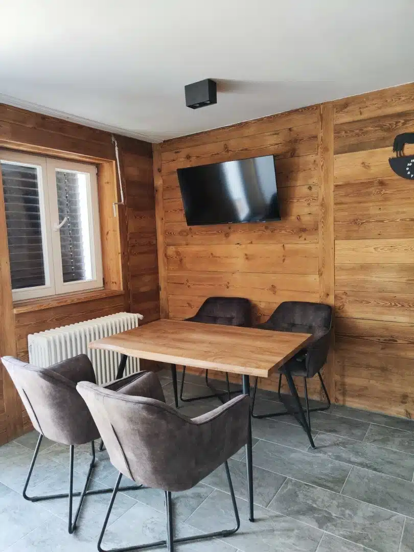 Pokój dzienny w apartamencie Ursa, Vigor Horses, z drewnianym stolikiem i nowoczesnymi krzesłami na tle drewnianych ścian, obok telewizora