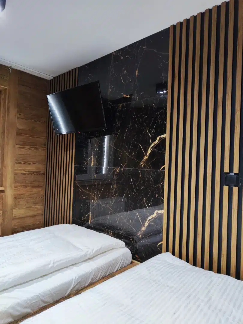 Modernistyczna sypialnia w apartamencie Ursa, Vigor Horses, z przestronnym telewizorem i eleganckimi czarnymi płytkami, które kontrastują z ciepłymi drewnianymi elementami